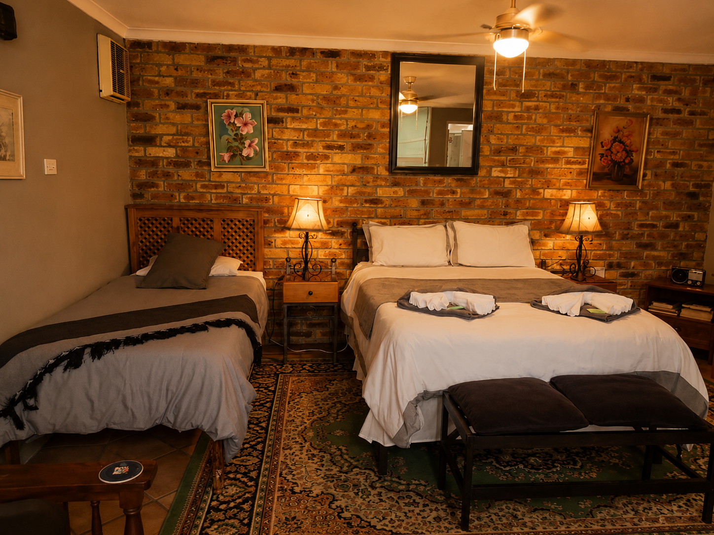 Hibiskus Suite sleeping area with double bed, single bed, bedside lamps and exposed brick feature wall